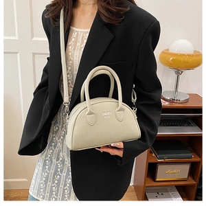 Detail of a beige textured leather shell handbag held by a model in a black blazer