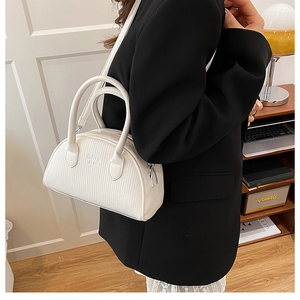 Detail of a creamy white minimalist shell handbag with leather texture and top handles
