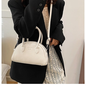 Close-up of a white textured shell bag with adjustable strap and twin handles on a model