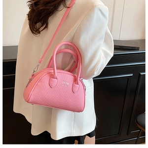 Pink pleated boston bag with top handles shown on a model wearing a white suit