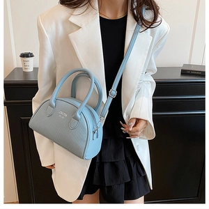 Close-up of a light blue textured Boston bag styled with a white blazer and black skirt
