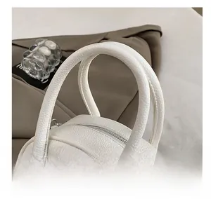 Detail view of white lychee leather handbag with smooth rounded handle and silver zipper