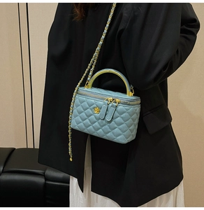 Detail of light blue quilted mini vanity bag with gold camellia accent and chain