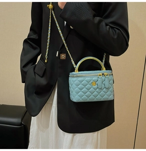 Detail of light blue quilted chain bag featuring a gold floral clasp and tubular handle