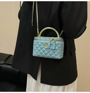 Macro detail of quilted light blue box bag with golden floral accent and metal handle