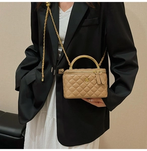 Detail of quilted box bag featuring a golden camellia logo and metal top handle