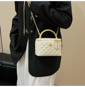 Detail of quilted beige box bag with gold floral clasp and metal chain strap