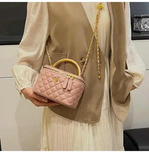 Pink quilted leather mini box bag with gold metal handle worn as a crossbody purse