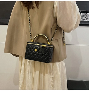 Detail of black quilted vanity bag with gold curved handle and leather chain strap