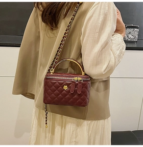 Detail view of burgundy quilted box bag with golden metal handle and chain strap