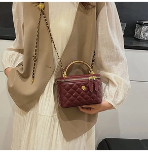 Detail of burgundy quilted box bag with golden floral logo and metal top handle