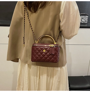 Detail of burgundy quilted vanity bag with golden semi-circular handle and floral charm