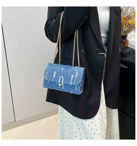Close-up of blue denim flap bag with distressed fraying details and golden chain strap