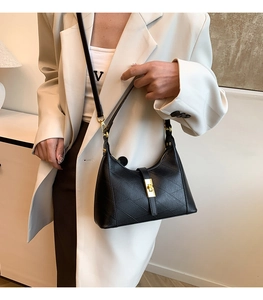 Close-up of black crossbody dumpling bag with gold hardware worn by a model in a suit