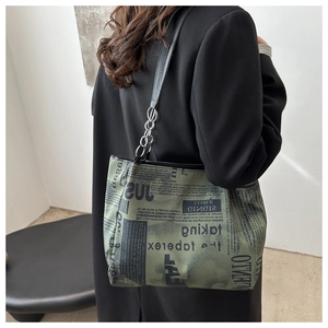 Detail of green newspaper print tote bag with black strap and silver chain on model