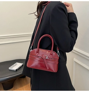 Detail of dark red shell-shaped handbag in glossy leather with decorative strap design
