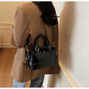 Detail of a shiny black leather pillow bag with gold hardware and white stitching