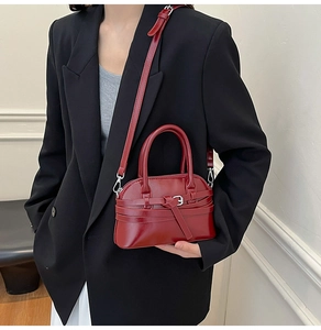 Detail of burgundy shell-shaped crossbody bag with belt buckle and silver hardware