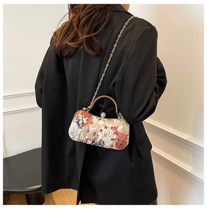 Detailed view of floral embroidery clutch with golden handle on black blazer background