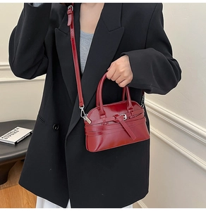 Detail of burgundy shell bag with shiny finish and belt buckle worn by a model