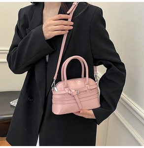 Detail of pink shell bag featuring triple decorative belts and silver buckles on matte leather