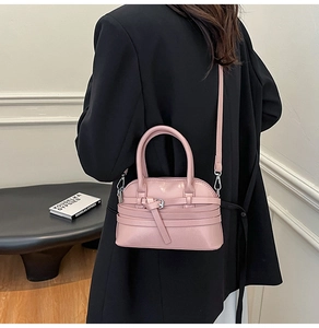 Model wearing a pink shell-shaped crossbody bag with belt strap detail and silver hardware