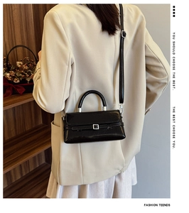 Detail of a black glossy crossbody bag featuring silver hardware and a belt buckle design