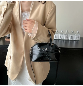 Fashionable black leather shell bag with belt buckle detail shown on a model
