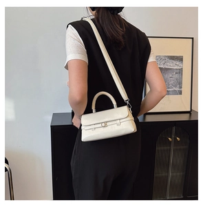 Detail of a minimalist cream white faux leather crossbody bag with buckle belt and top handle
