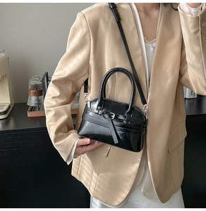 Detail of glossy black shell handbag with buckle strap on a model wearing beige blazer