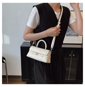 Detail of a creamy white crossbody bag with glossy finish and metal buckle closure