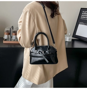 Polished black shell bag shown on model with beige blazer and white satin dress
