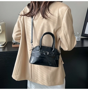 Close-up of black shell-shaped crossbody bag with decorative silver buckle on model