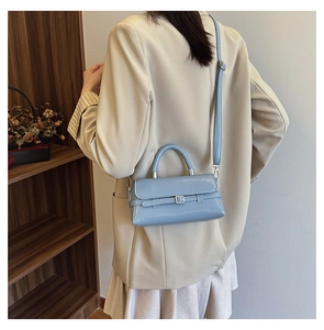 Light blue glossy crossbody bag with metal buckle shown on model in modern home setting