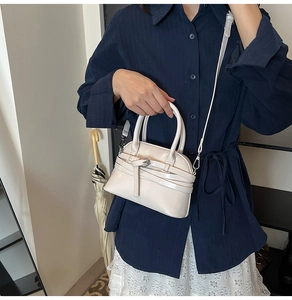Fashionable cream shell bag with decorative belt detail and polished finish held by a model