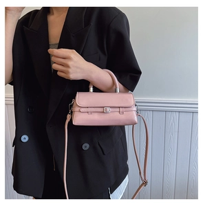 Close-up of a pink leather crossbody bag with metal buckle worn by a model in a suit