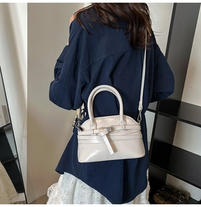 Detail of cream shell bag featuring smooth leather texture and metal buckle accents