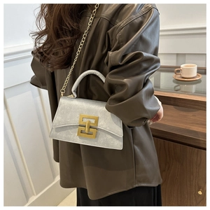 Sac bandoulière gris argenté avec chaîne dorée porté par un modèle dans un décor de café
