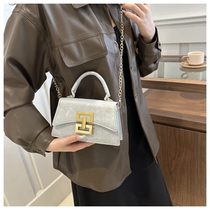 Détail du sac bandoulière gris argenté avec fermoir doré sur texture cuir souple