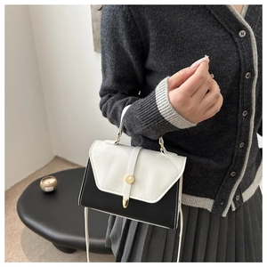 Close-up of black and white leather crossbody bag featuring a golden circular metal lock