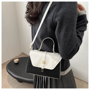 Detail of a minimalist black and white crossbody bag with a round gold buckle on a model