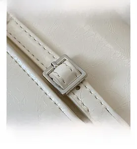 Detail of silver square metal buckle and white textured leather on a minimalist handbag