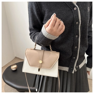 Detail of color-block PU leather crossbody bag with round gold buckle on gray cardigan