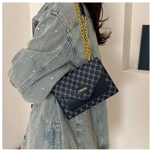 Détail du motif géométrique rétro et de la chaîne dorée sur un sac à rabat noir