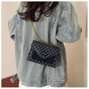 Détail du sac bandoulière gris à monogramme avec chaîne dorée et étiquette sur veste en jean