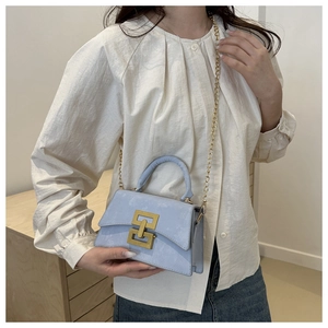 Sac bandoulière bleu clair avec boucle dorée et bandoulière chaîne porté par mannequin
