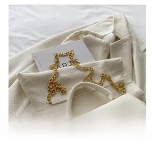 Détail d'un sac bandoulière blanc texturé avec chaîne dorée et boucle à verrouillage
