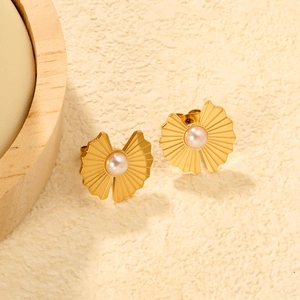 Détail de boucles d'oreilles dorées en forme d'éventail avec perle sur fond texturé