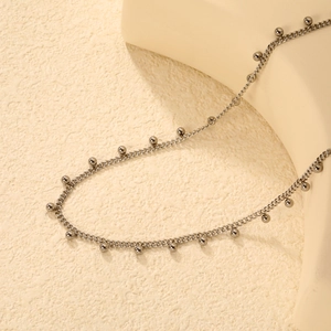Close-up of a silver beaded chain necklace draped over a minimalist display stand