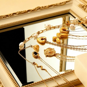Colliers dorés avec pendentifs papillon et perle sur une surface miroir vintage